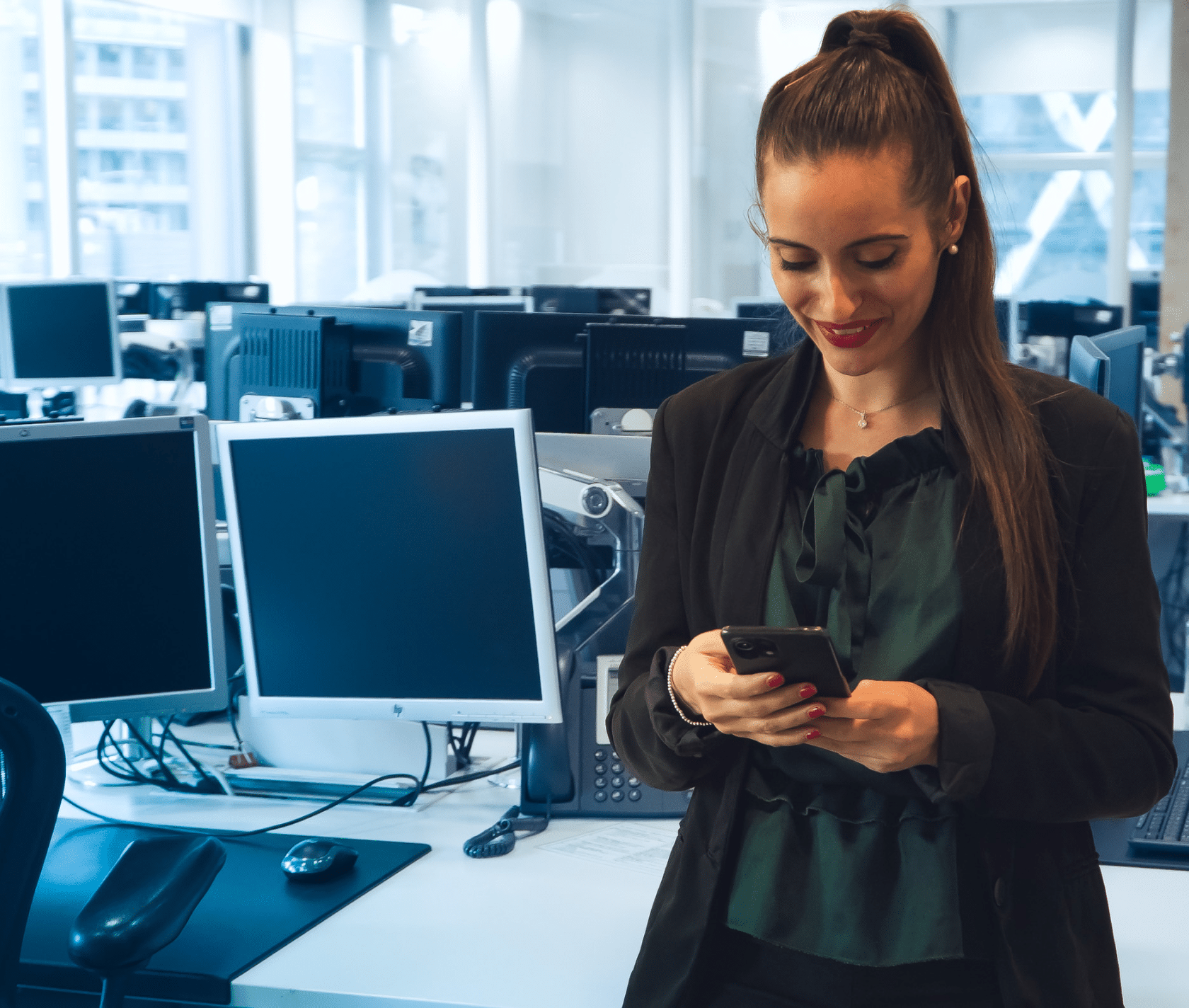 a woman in financial services is looking at her phone and smiling in the office